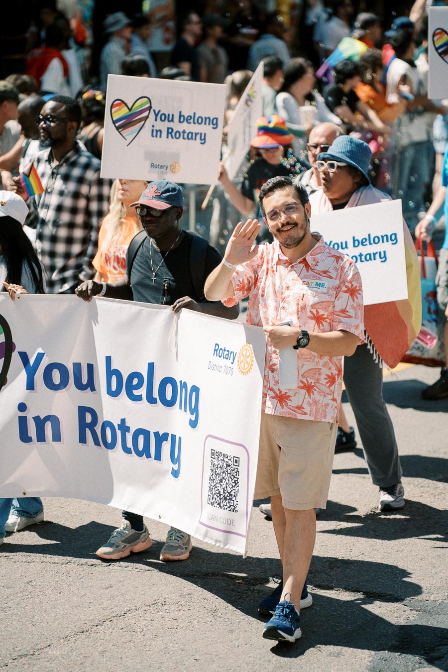 Participants in a parade hold signs promoting inclusivity in Rotary, with messages like 'You belong in Rotary'.