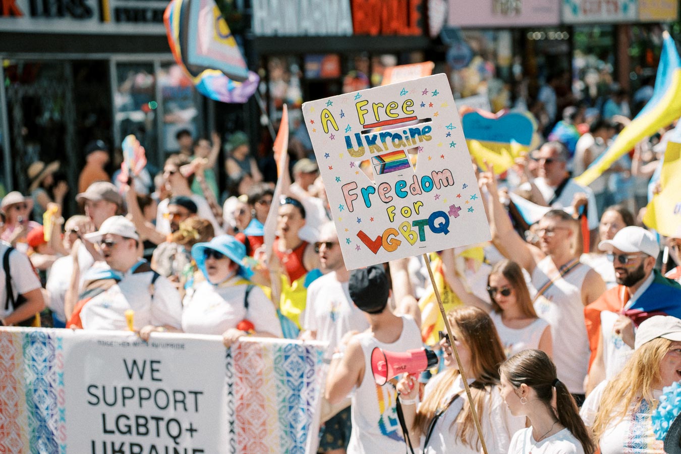 Participants at a pride parade hold signs advocating for LGBTQ+ rights and a free Ukraine.