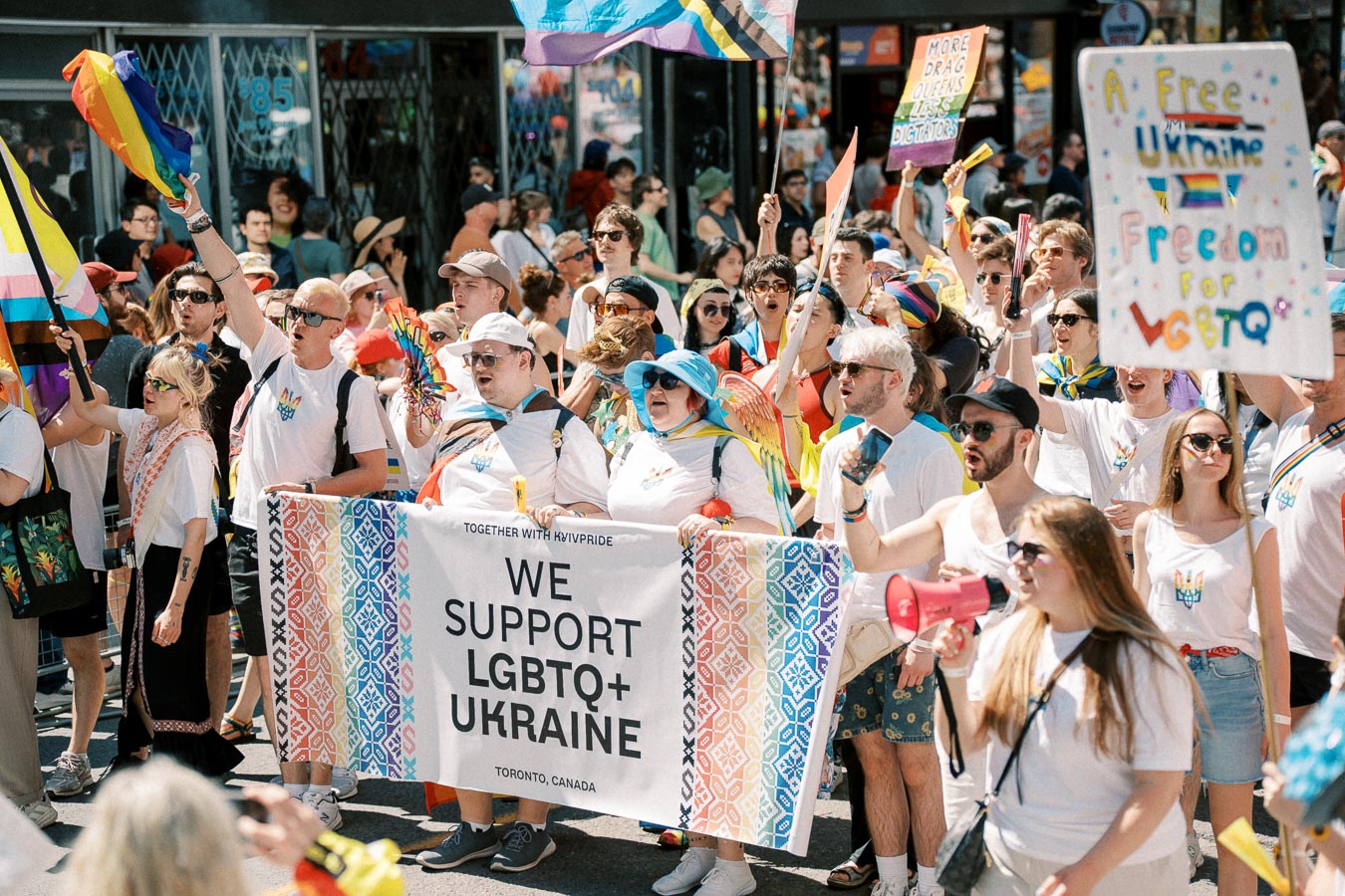 Participants in a pride parade hold a banner supporting LGBTQ+ rights in Ukraine, with colorful flags and signs.