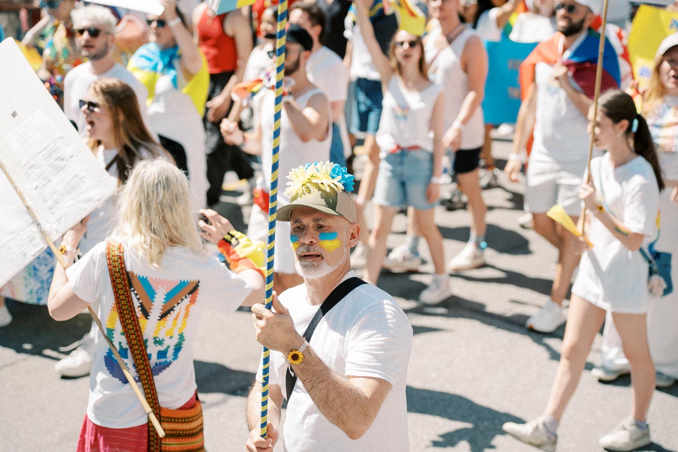 Participants in a vibrant parade, dressed in white with colorful accents, celebrate with flags and flowers.