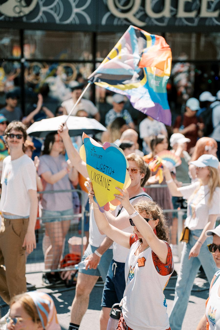 Participants in a pride parade show support for LGBTQ+ rights in Ukraine, holding a colorful sign and waving a rainbow flag.