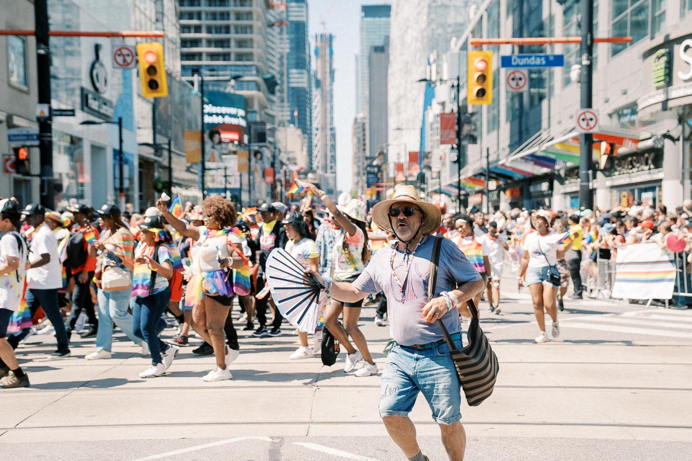 Participants in a vibrant parade march down a city street, celebrating diversity with rainbow-themed attire and flags.