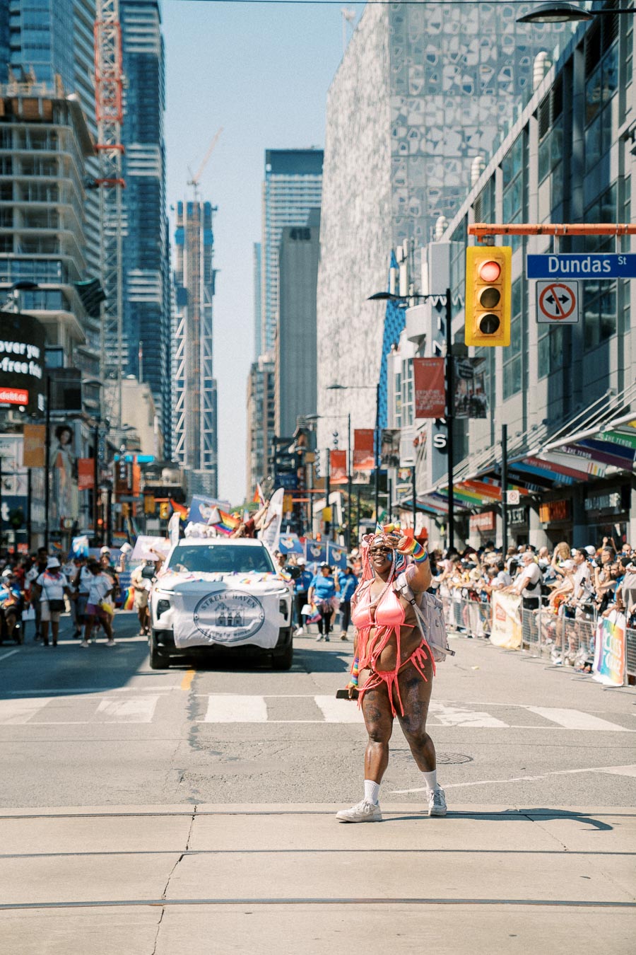 A vibrant parade on Dundas Street featuring a person in colorful attire and a decorated vehicle, with spectators lining the street.