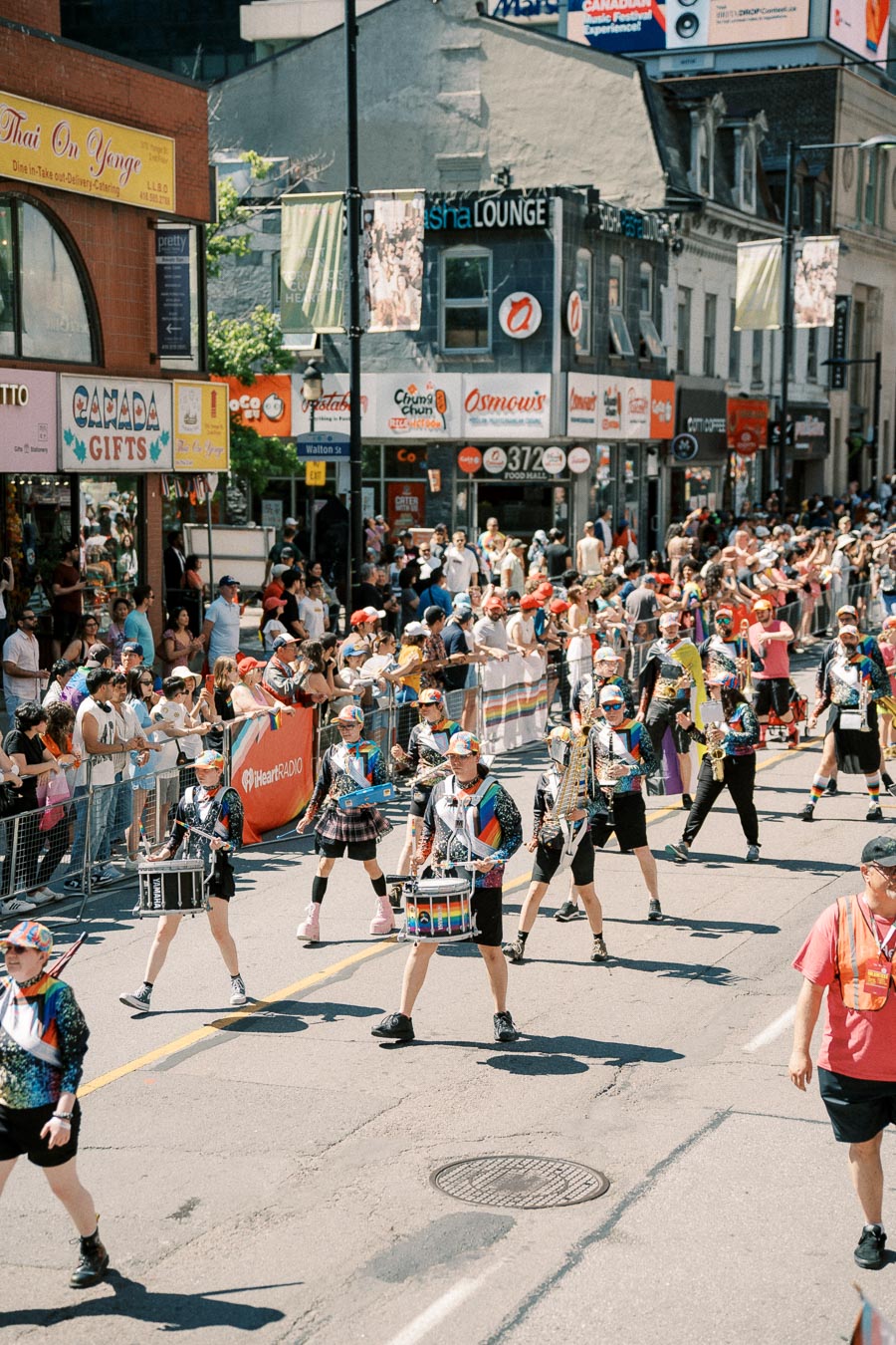 A vibrant parade featuring musicians in colorful attire marches through a bustling city street, with enthusiastic spectators watching from the sidelines.