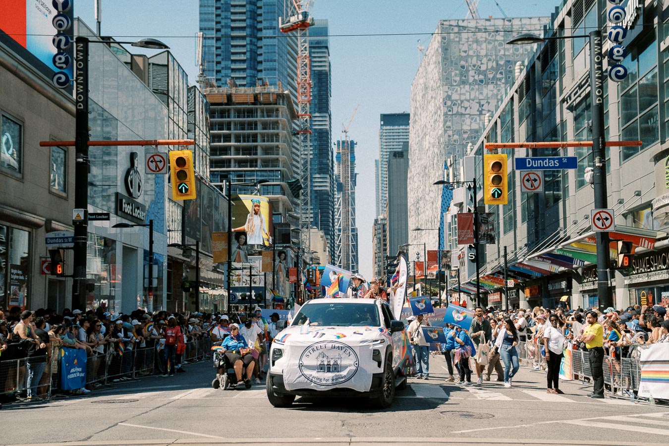 A vibrant parade on Dundas Street in Toronto, featuring a decorated vehicle and a lively crowd.