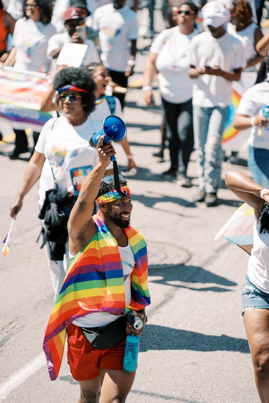 Participants in a pride parade celebrate with rainbow flags and megaphones, promoting LGBTQ+ pride and visibility.