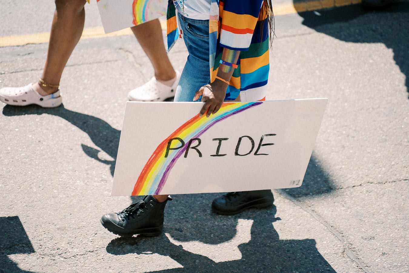 A person participates in a pride parade, holding a sign with a rainbow and the word 'PRIDE'.