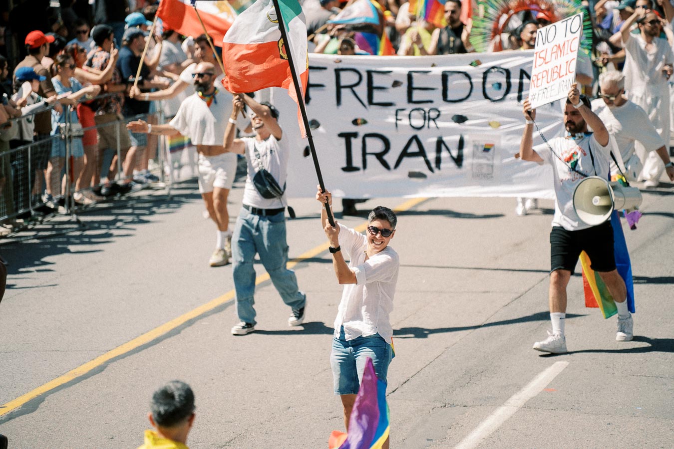 Participants in a parade advocating for freedom in Iran, holding signs and flags.
