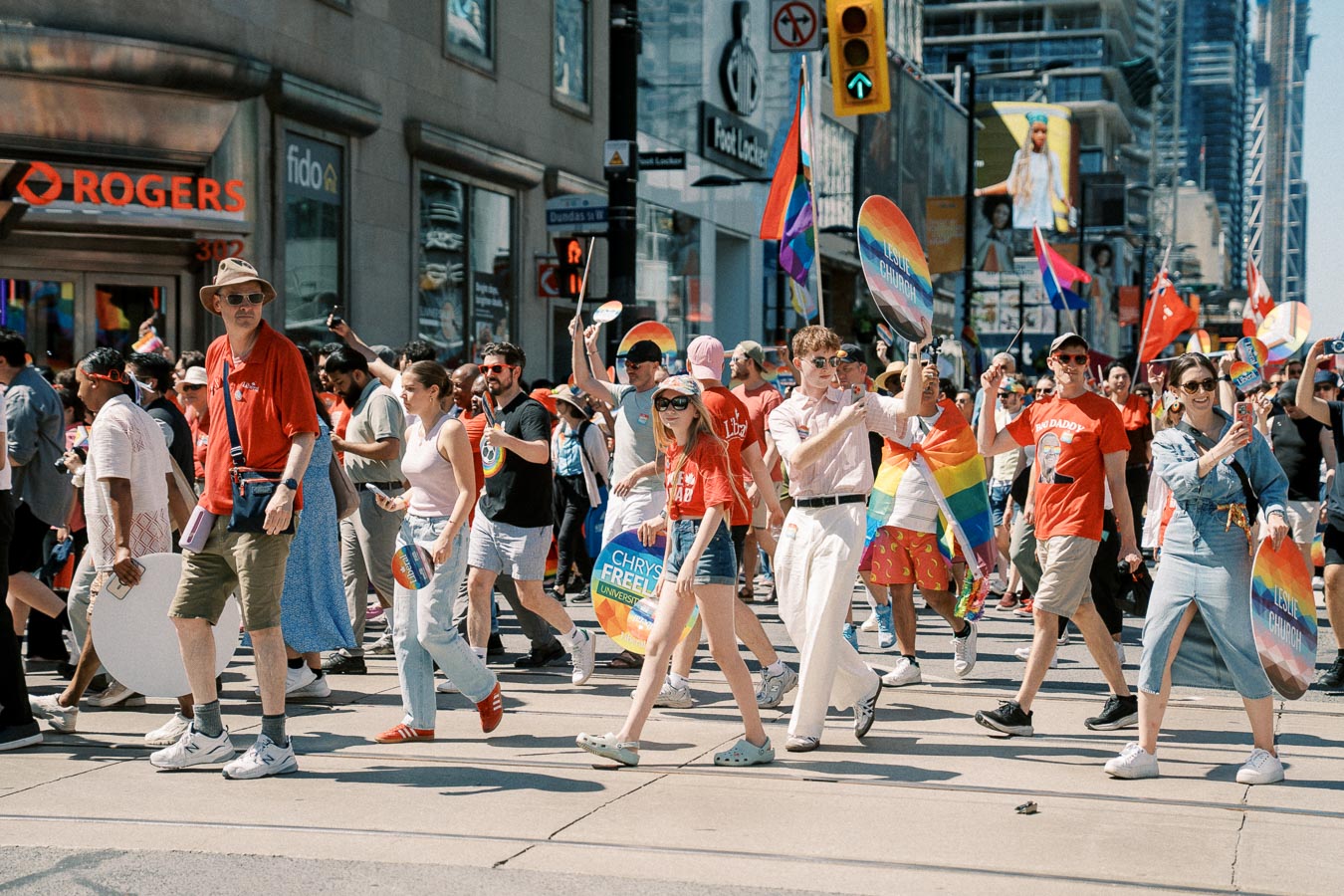 Participants in a pride parade march through a city street, displaying rainbow flags and signs, celebrating diversity and inclusion.