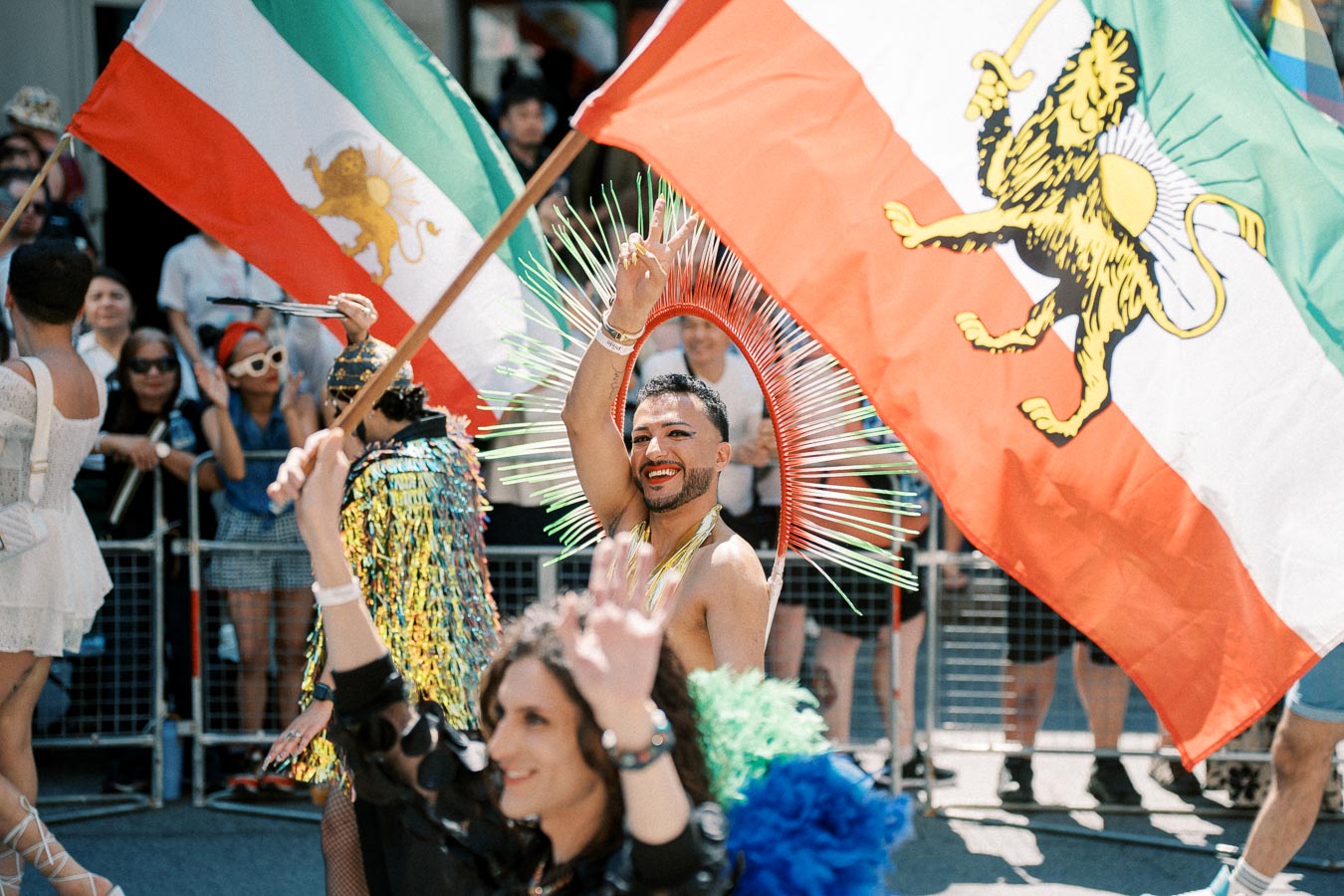 A participant in a vibrant costume waves a flag featuring a lion emblem during a lively parade.