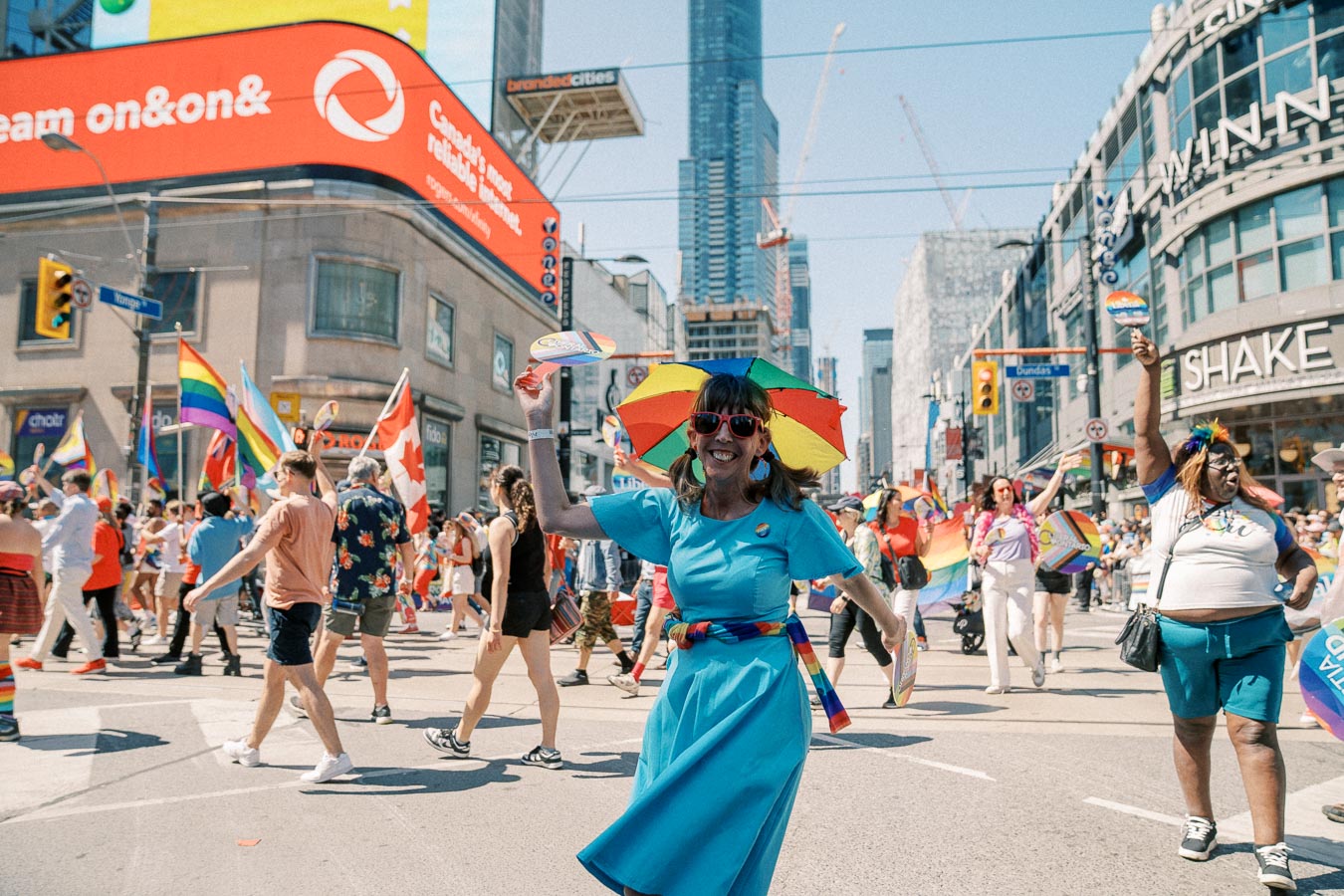 Participants celebrate at a pride parade in Toronto, showcasing colorful flags and attire against the backdrop of the city's skyscrapers.