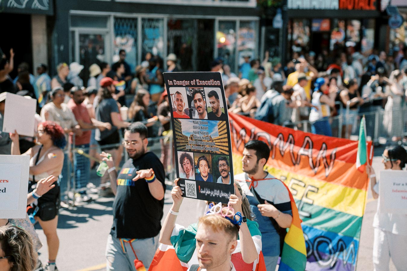 Participants in a parade advocating for human rights and LGBTQ+ rights, holding signs and banners, including one highlighting individuals in danger of execution.