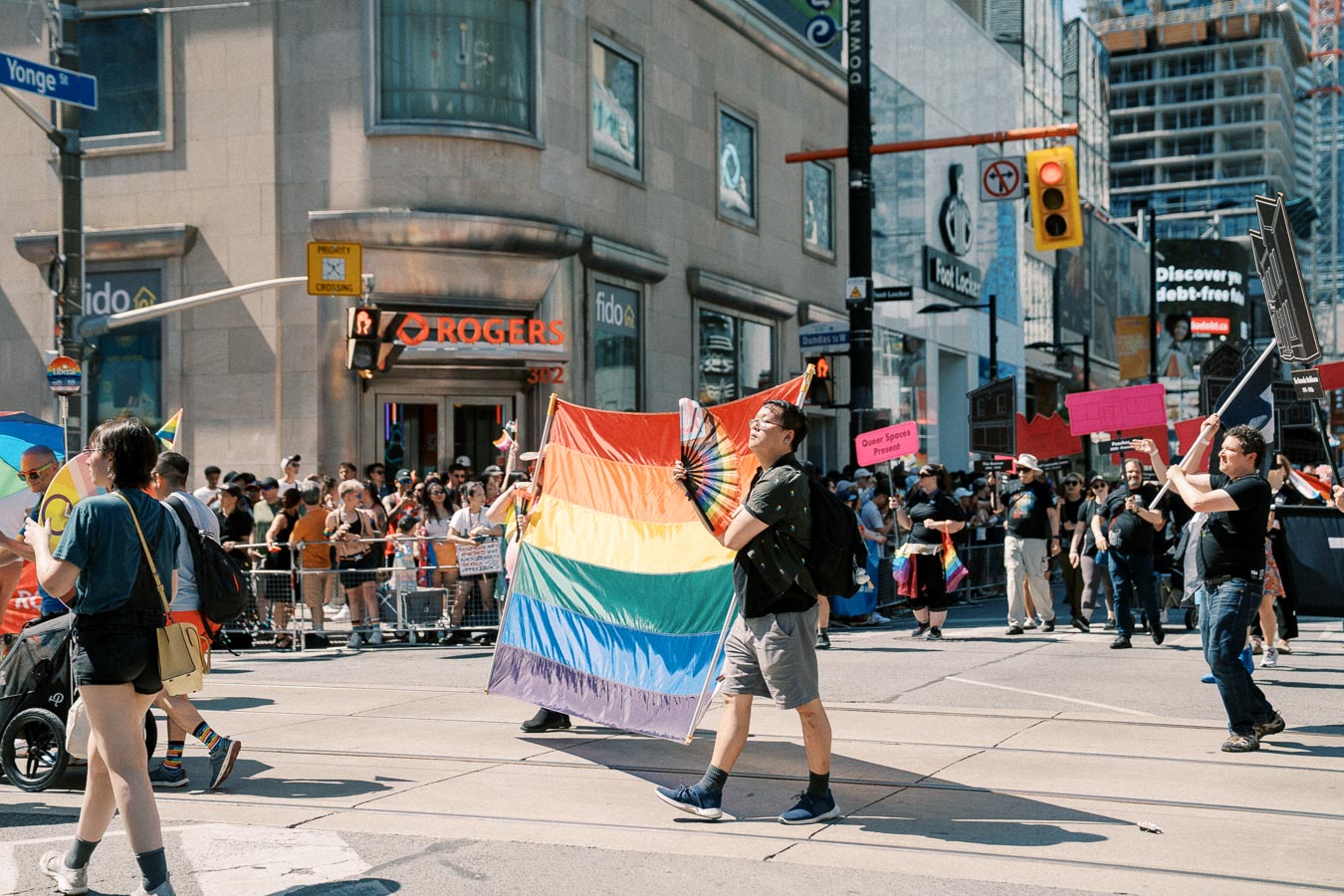Participants in a pride parade march with rainbow flags and signs, celebrating diversity and inclusion in an urban setting.