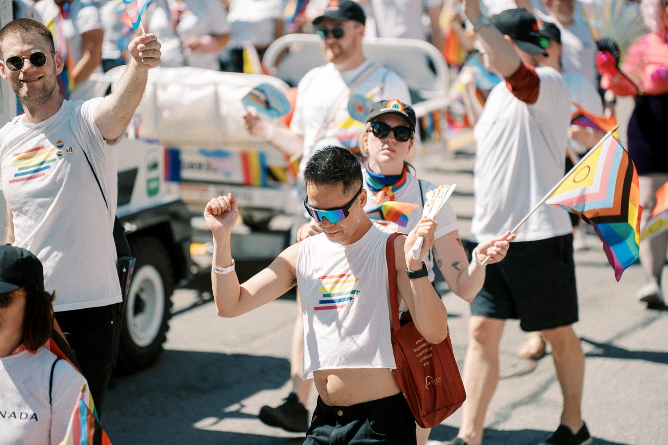 Participants celebrate at a pride parade, waving flags and wearing rainbow-themed attire.