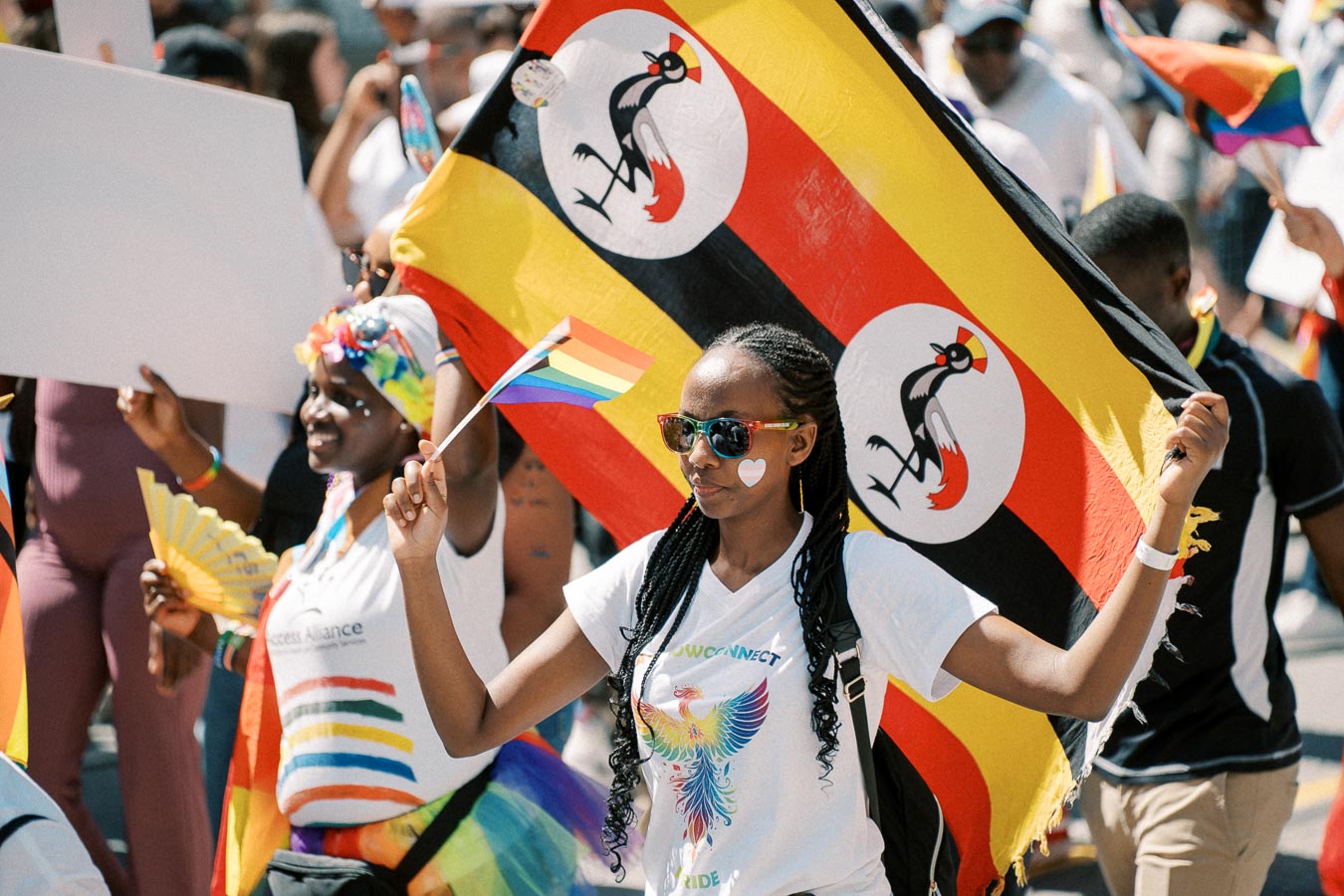 Participants at a pride parade hold a Ugandan flag and rainbow flags, celebrating diversity and inclusion.