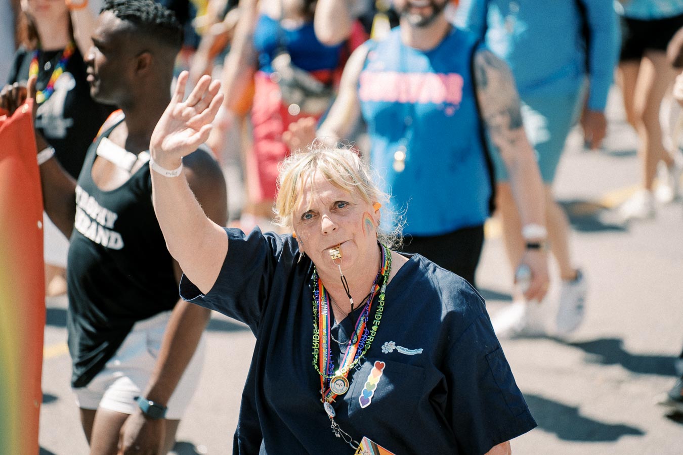 A person participates in a parade, wearing a whistle and rainbow-themed accessories, symbolizing LGBTQ+ pride.