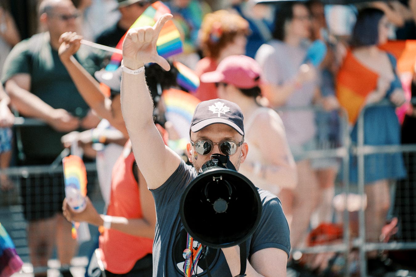 A person with a megaphone participates in a pride parade, surrounded by a crowd waving rainbow flags.