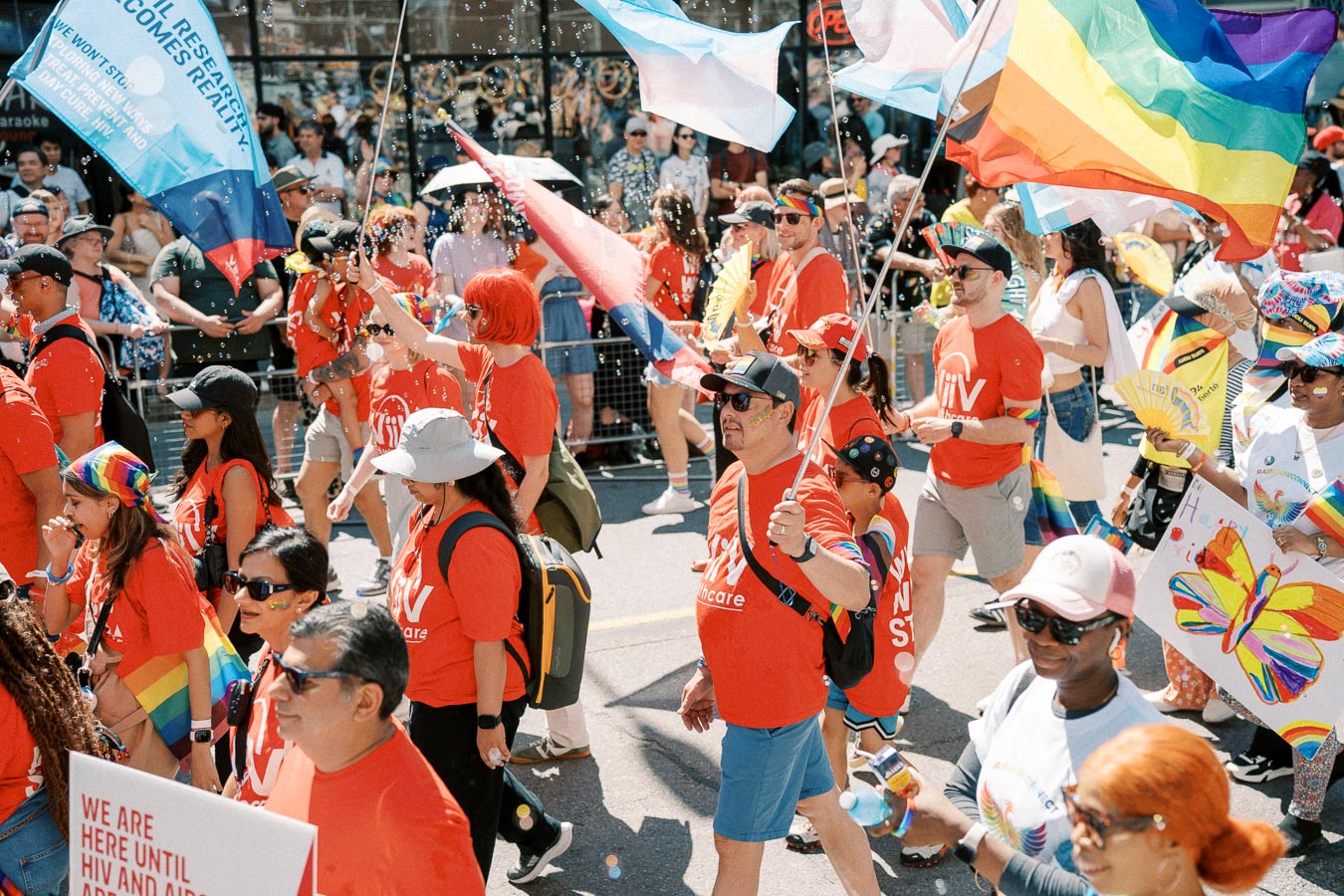 Participants in a lively parade wearing red shirts and carrying rainbow flags, celebrating diversity and inclusion.