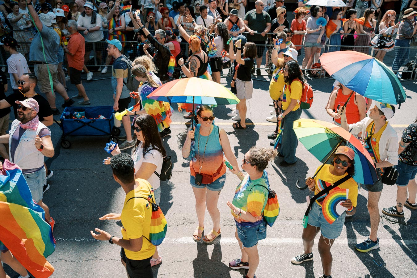 Participants at a pride parade joyfully celebrate with rainbow umbrellas and flags, surrounded by a lively crowd.
