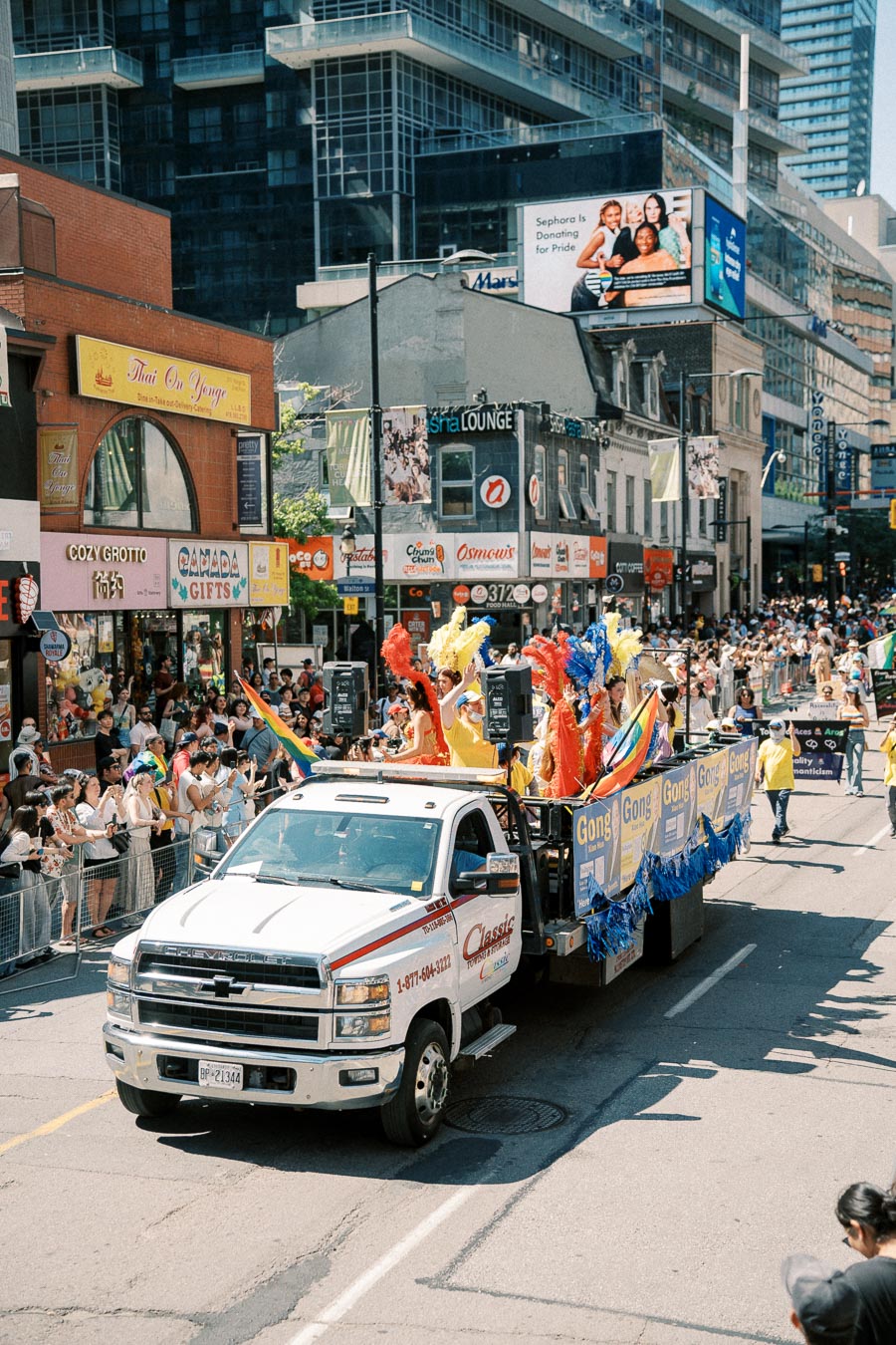 A vibrant parade float moves down a city street, featuring people in colorful costumes and surrounded by cheering spectators.