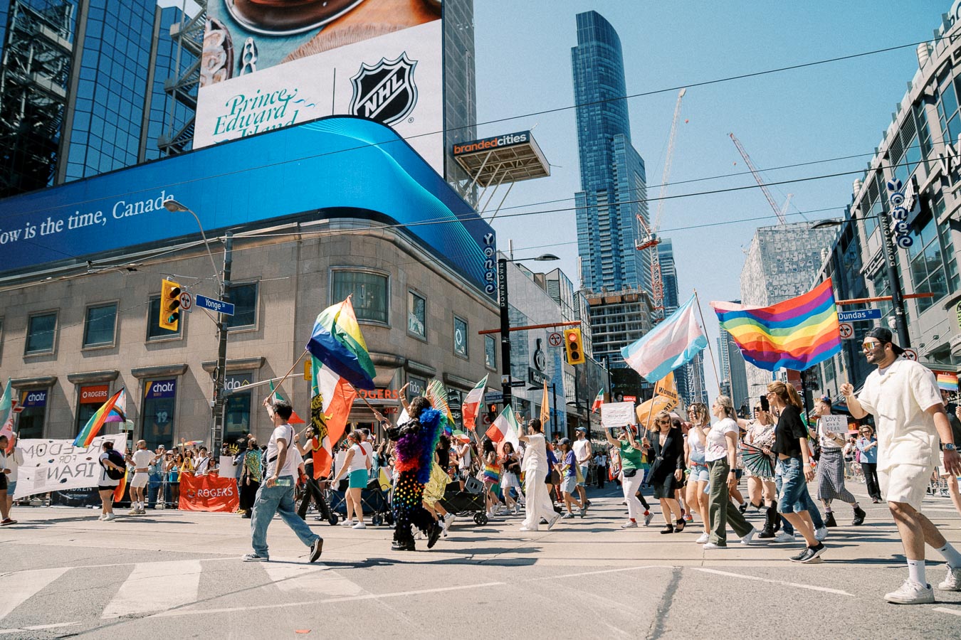 A lively parade featuring rainbow flags and banners at a bustling city intersection, showcasing a celebration of diversity and inclusion.