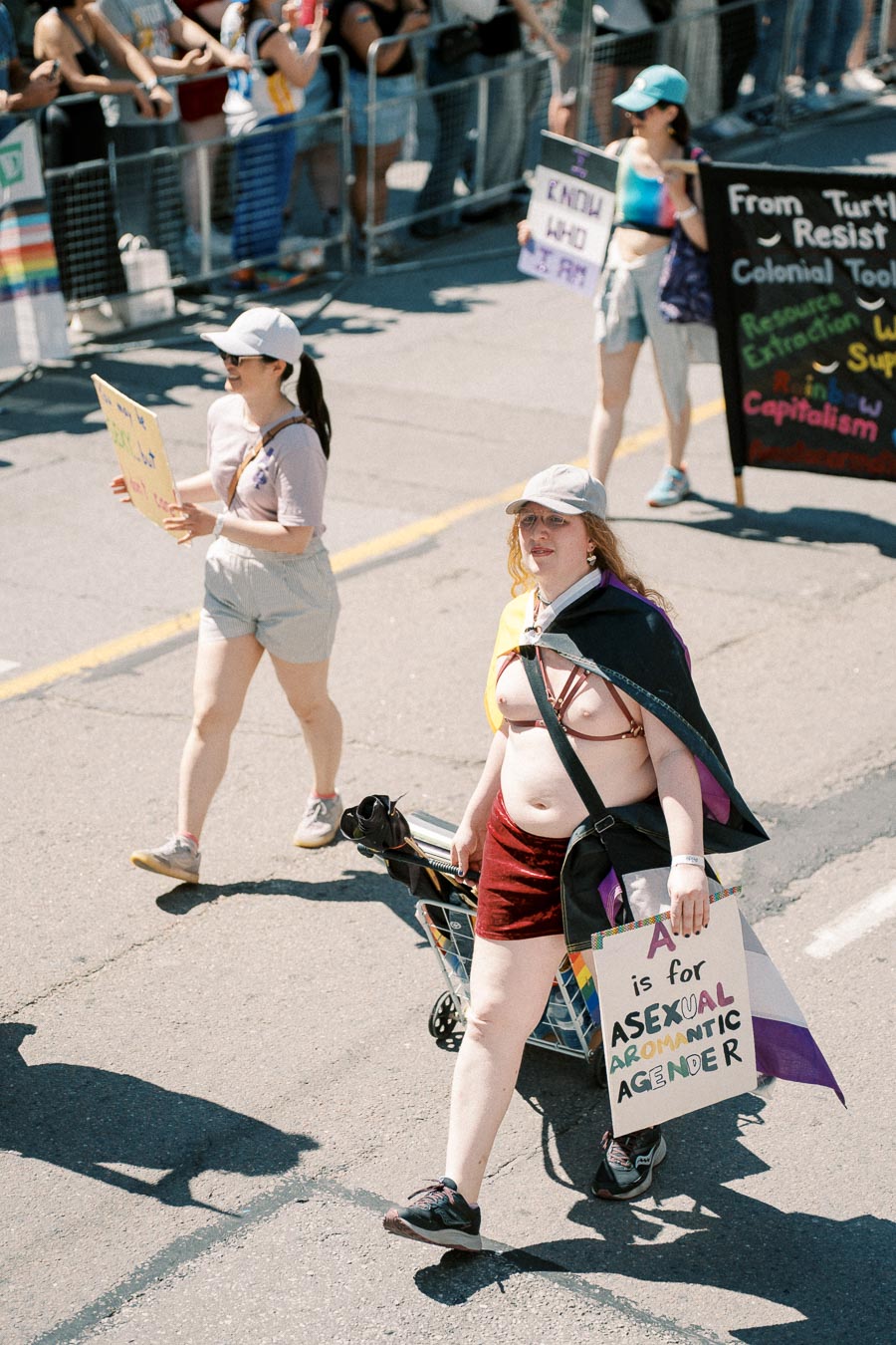 Participants in a pride parade hold signs advocating for asexual, aromantic, and agender identities.