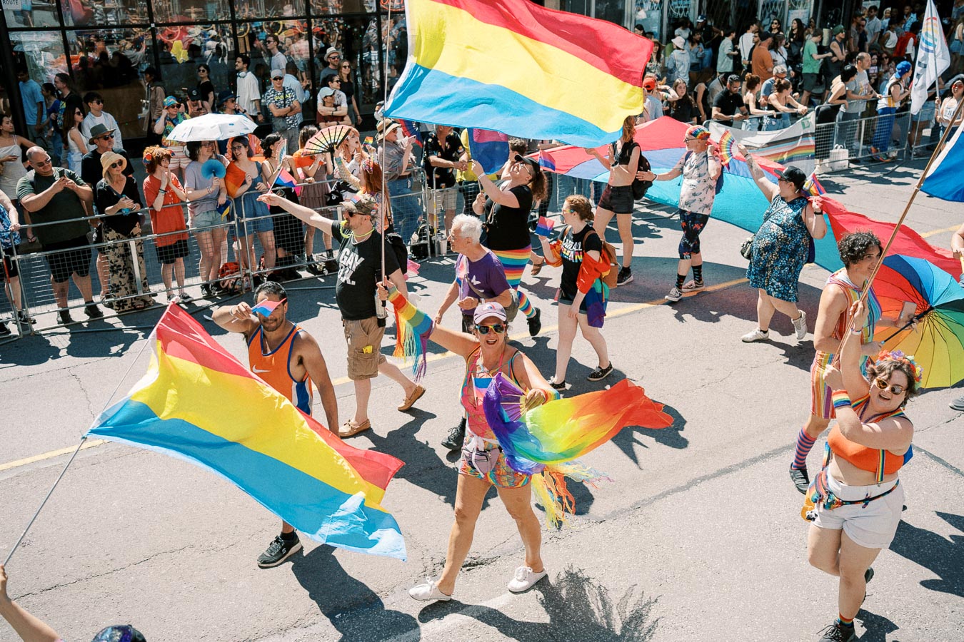 Participants in a pride parade wave rainbow and pansexual flags, celebrating diversity and inclusion.
