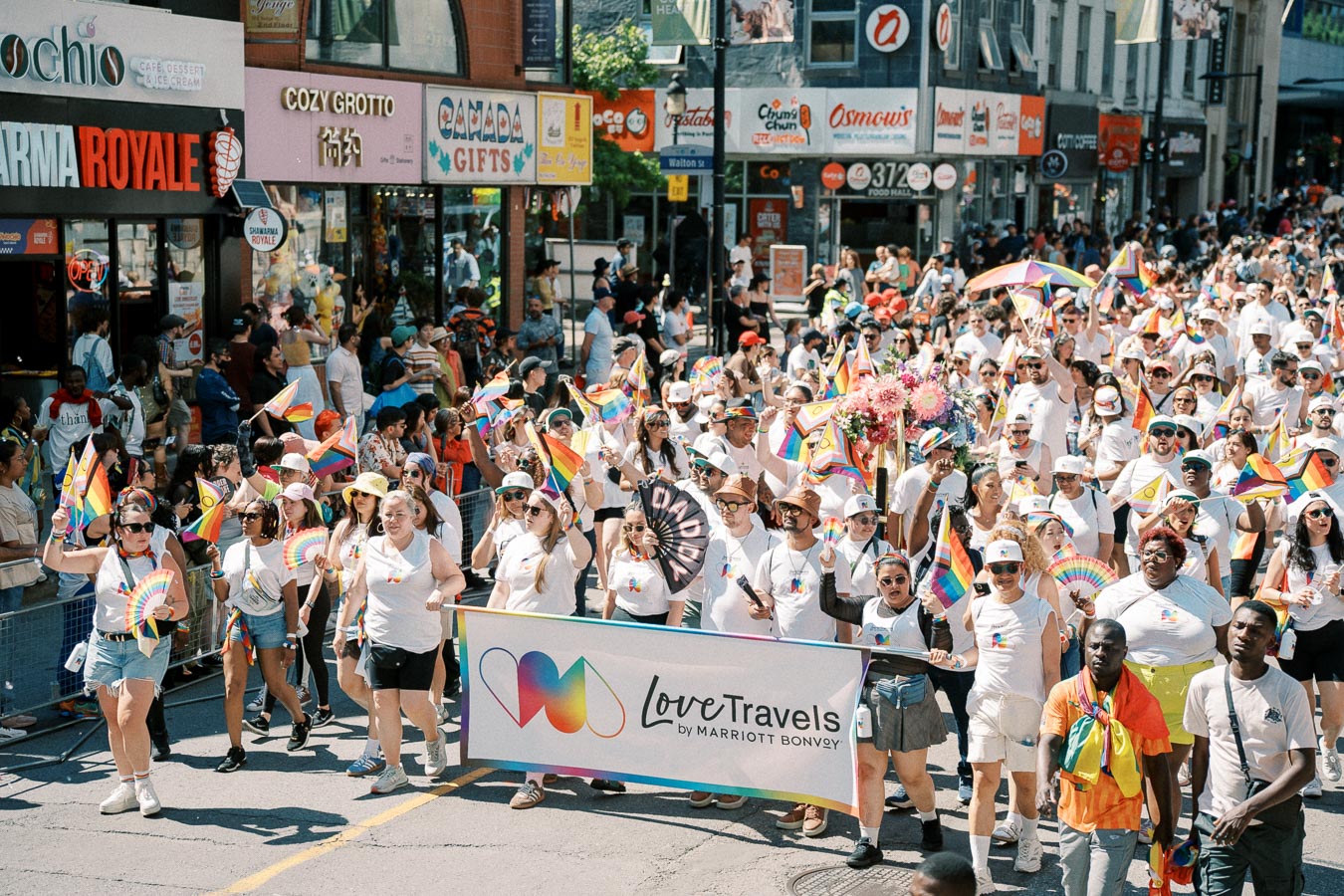 Participants in a pride parade march with rainbow flags and a 'Love Travels by Marriott Bonvoy' banner, celebrating diversity and inclusion.