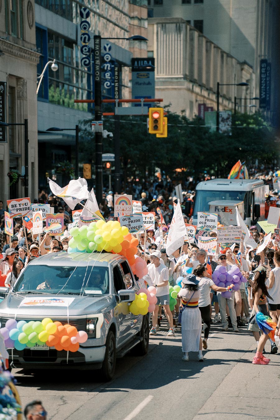 Participants in a pride parade march down a city street, holding signs and balloons, celebrating diversity and inclusion.