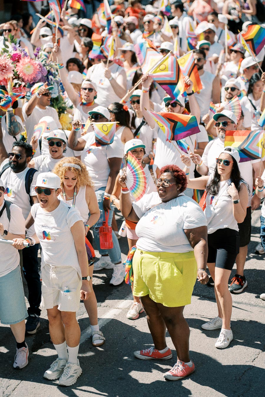 A vibrant pride parade with participants wearing white and waving rainbow flags, celebrating diversity and inclusion.