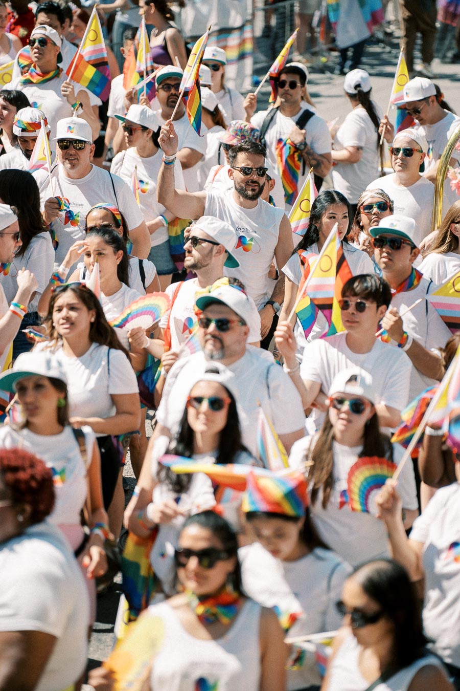 Participants at a pride parade wearing white shirts and waving rainbow flags, celebrating diversity and inclusion.