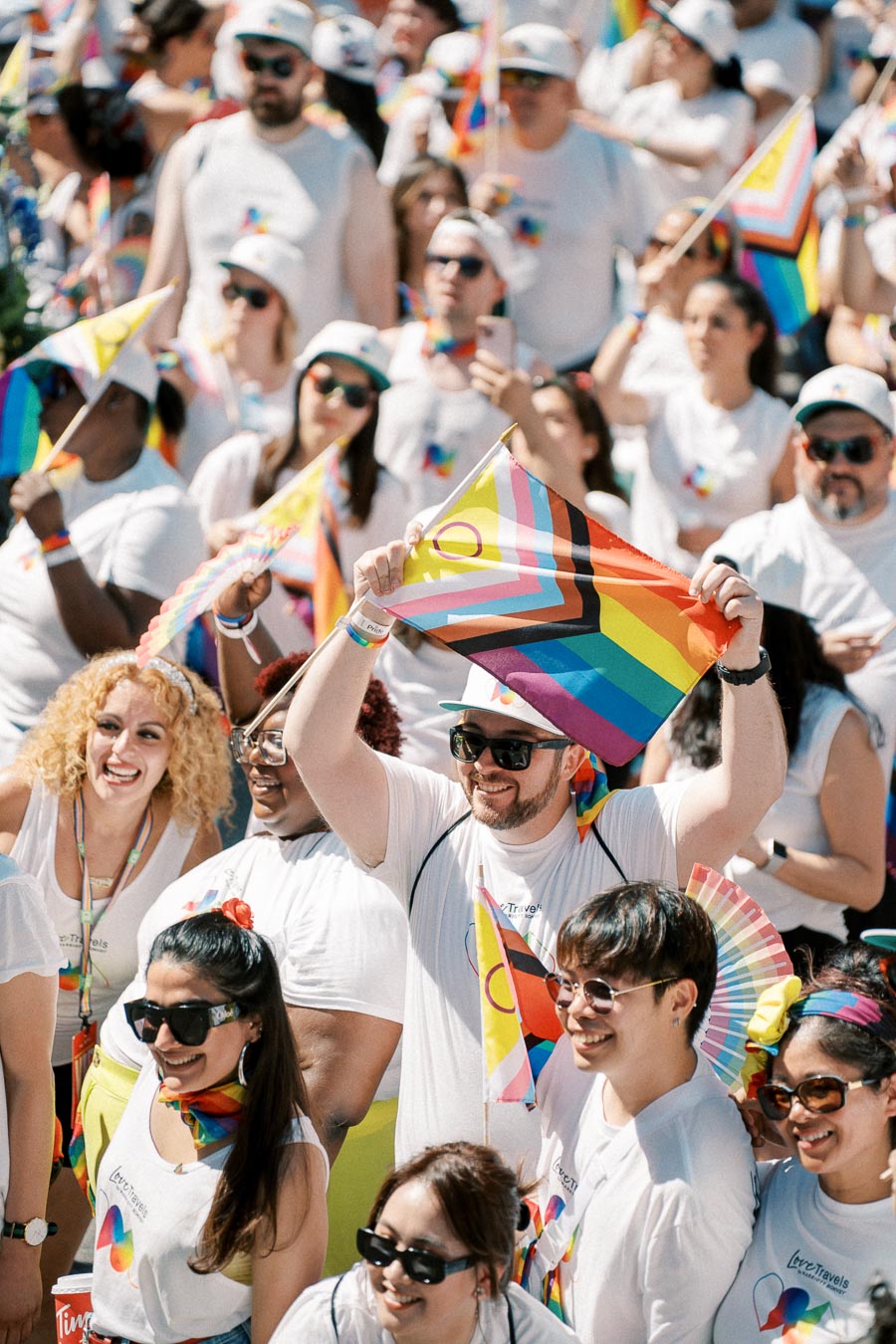 A vibrant crowd celebrates at a Pride parade, showcasing diversity and unity with rainbow flags and colorful attire.