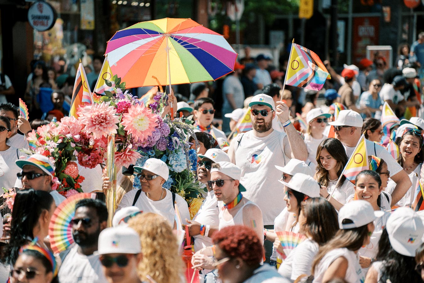 Participants at a pride parade celebrate with rainbow flags, colorful umbrellas, and vibrant floral decorations.
