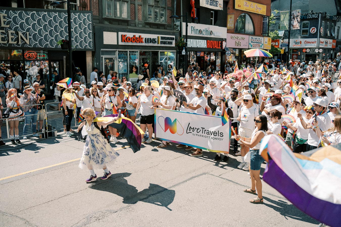 Participants in a pride parade hold rainbow flags and a 'Love Travels by Marriott Bonvoy' banner, celebrating diversity and inclusion.