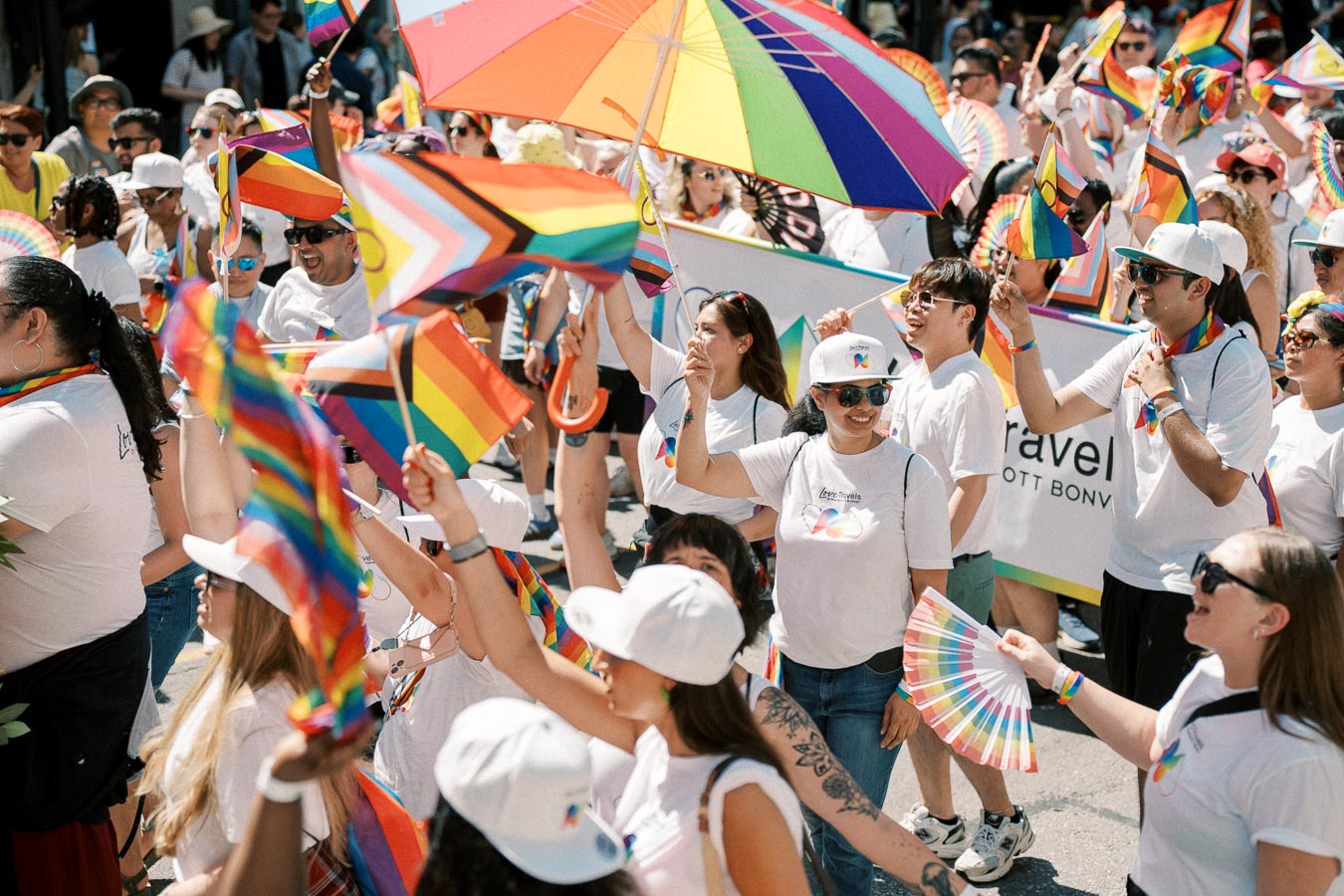 Participants at a Pride parade joyfully wave rainbow flags and umbrellas, celebrating diversity and inclusion.
