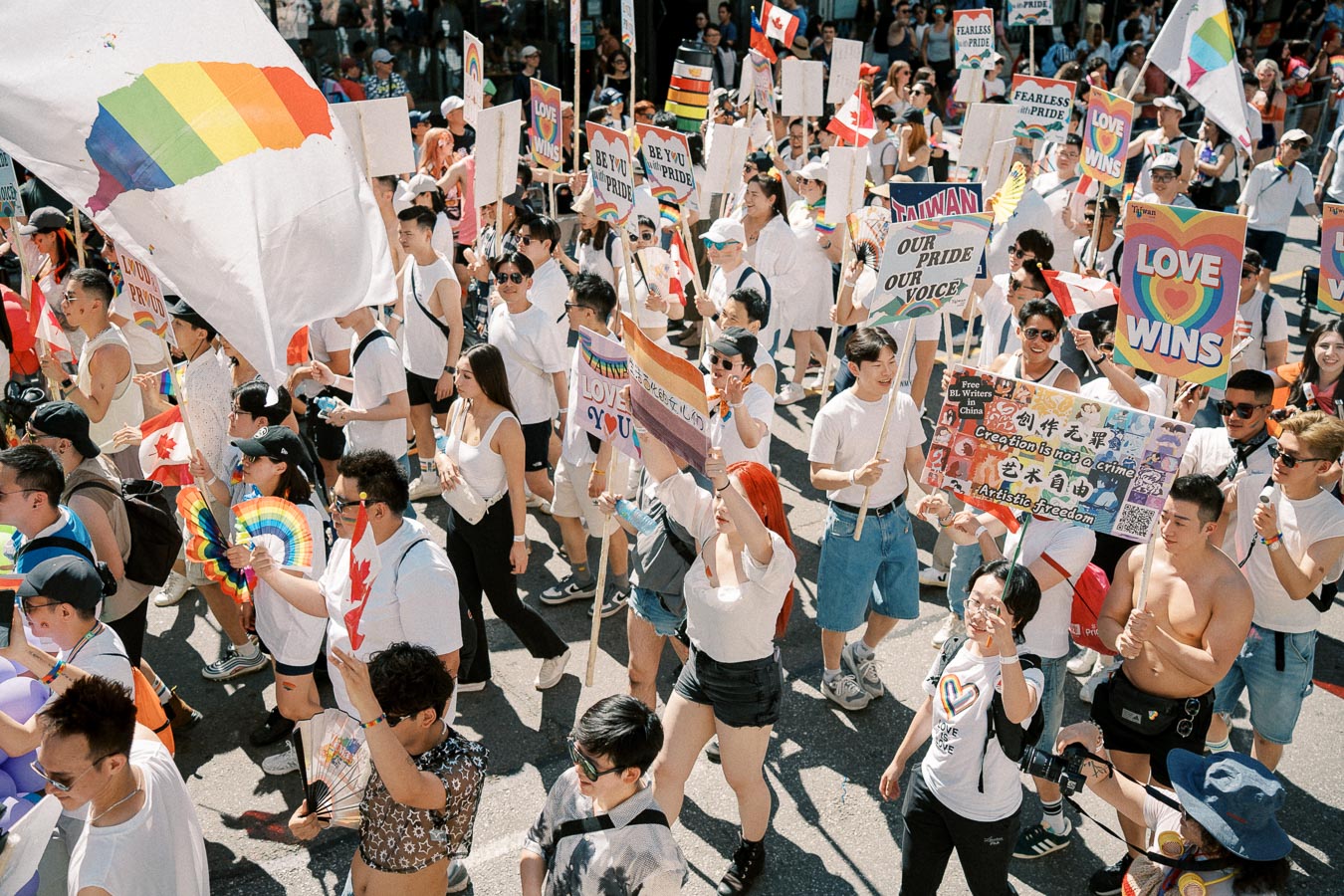 Participants in a pride parade march with rainbow flags and signs promoting love and equality.