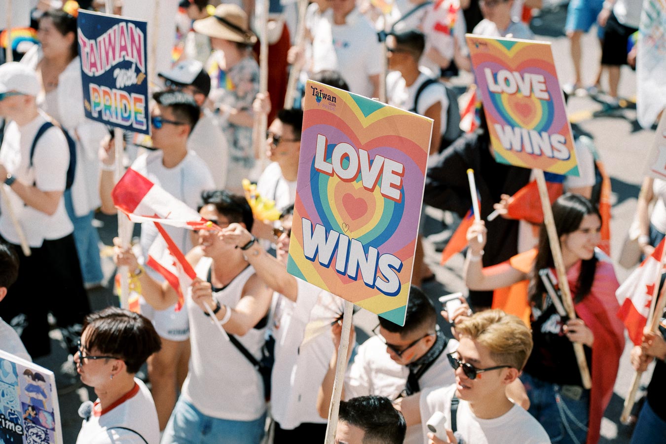 Participants at a pride parade hold colorful signs with messages like 'LOVE WINS' and 'TAIWAN WITH PRIDE'.