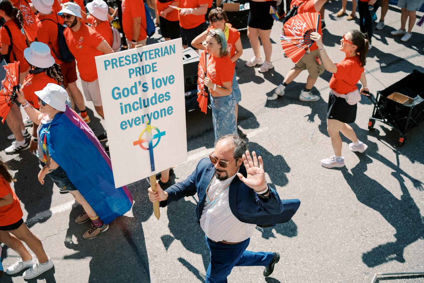 A participant in a parade holds a sign promoting inclusivity, surrounded by others in red attire.