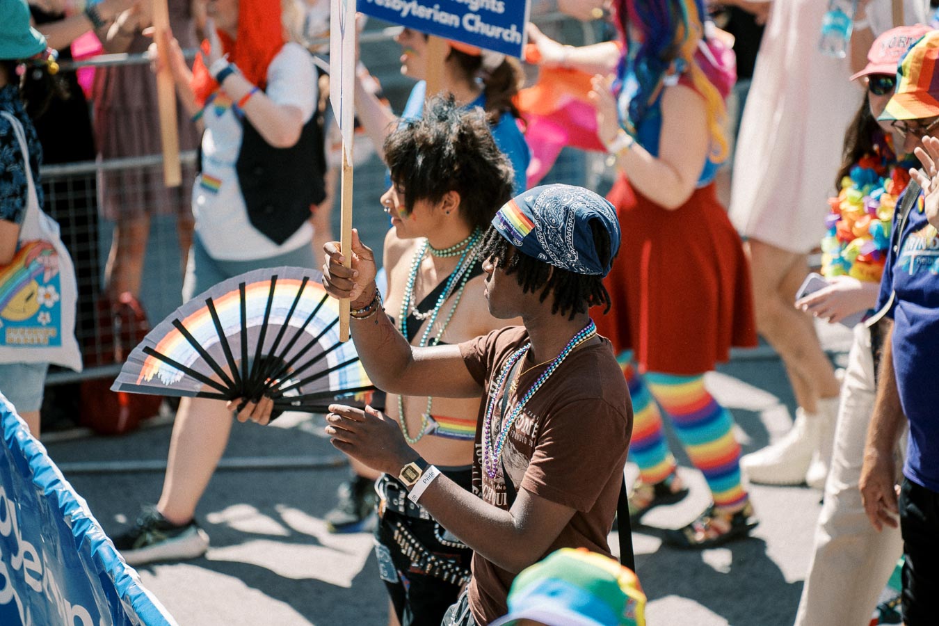 Participants in a pride parade celebrate with colorful attire and rainbow-themed accessories.
