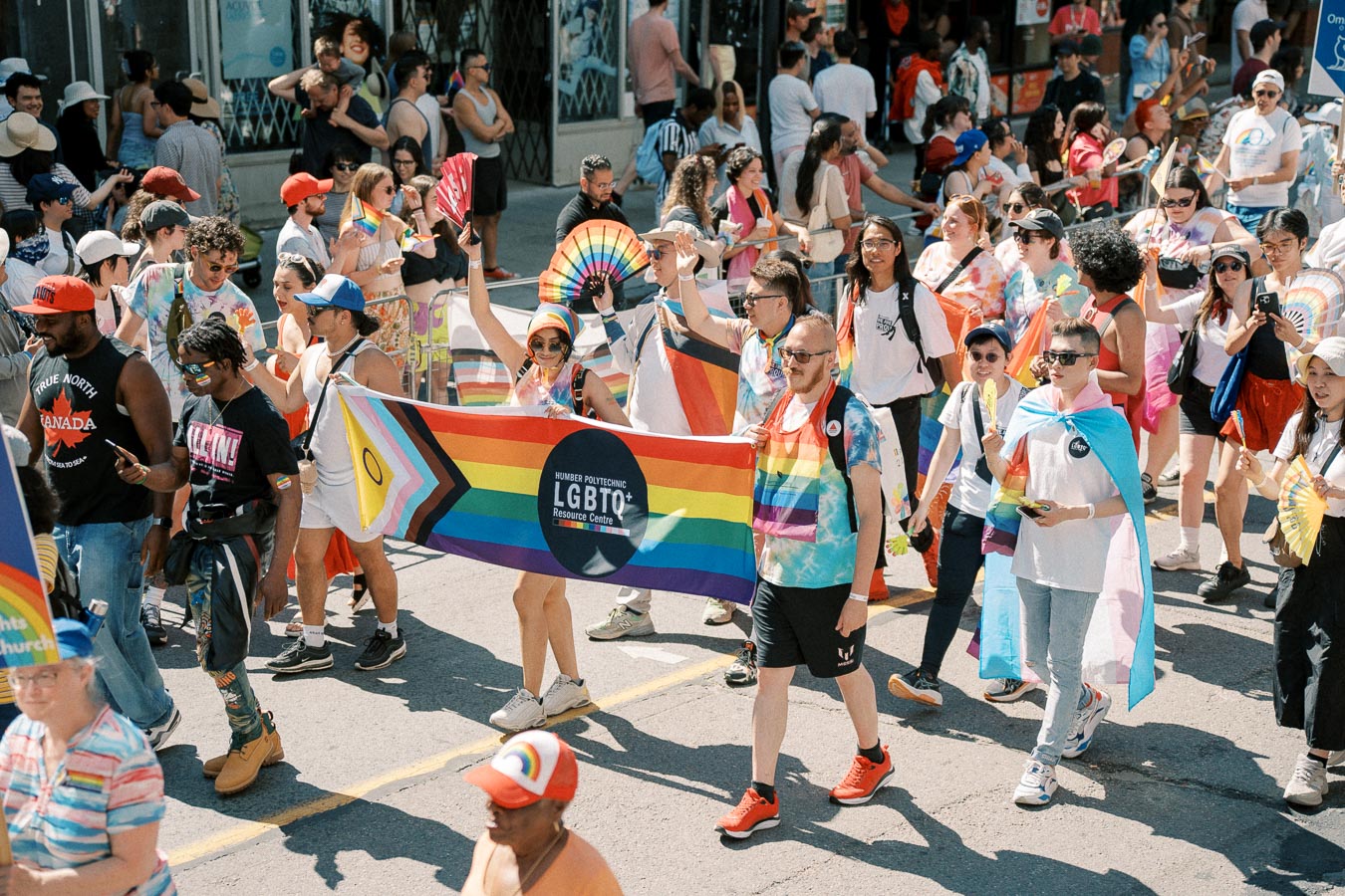 Participants in a pride parade celebrate diversity and inclusion, holding a rainbow flag and wearing vibrant attire.
