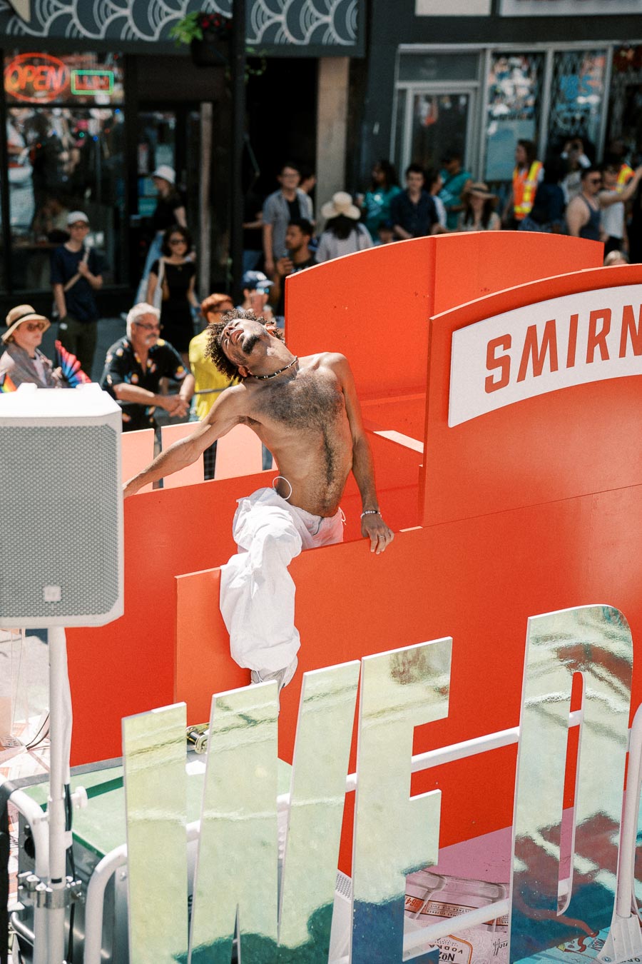 A lively scene at a parade featuring a dancer on a float with a prominent Smirnoff sign, surrounded by an enthusiastic crowd.
