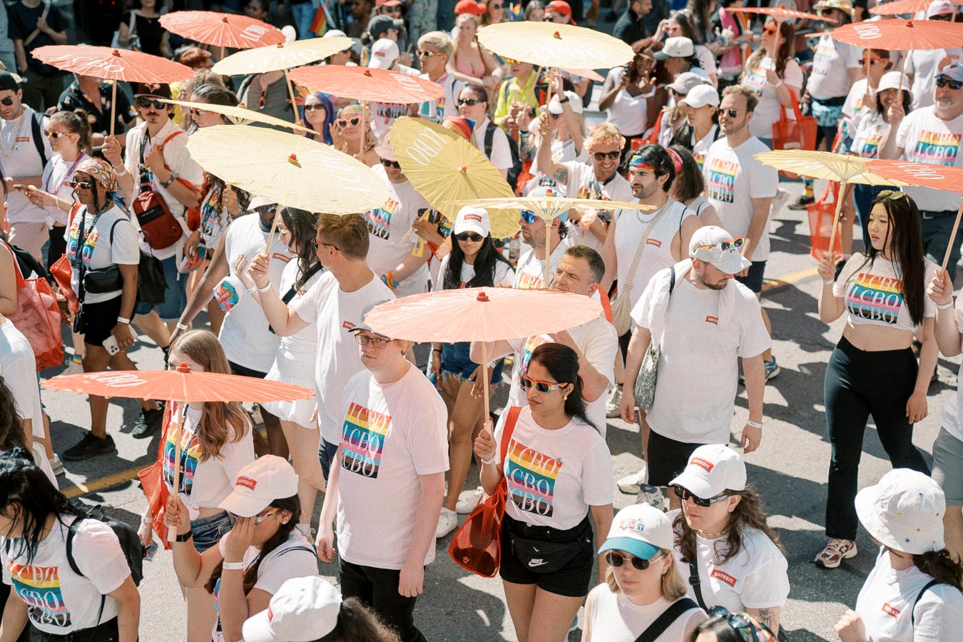 Participants in a parade wearing white shirts with rainbow designs and holding colorful parasols, celebrating diversity and inclusion.