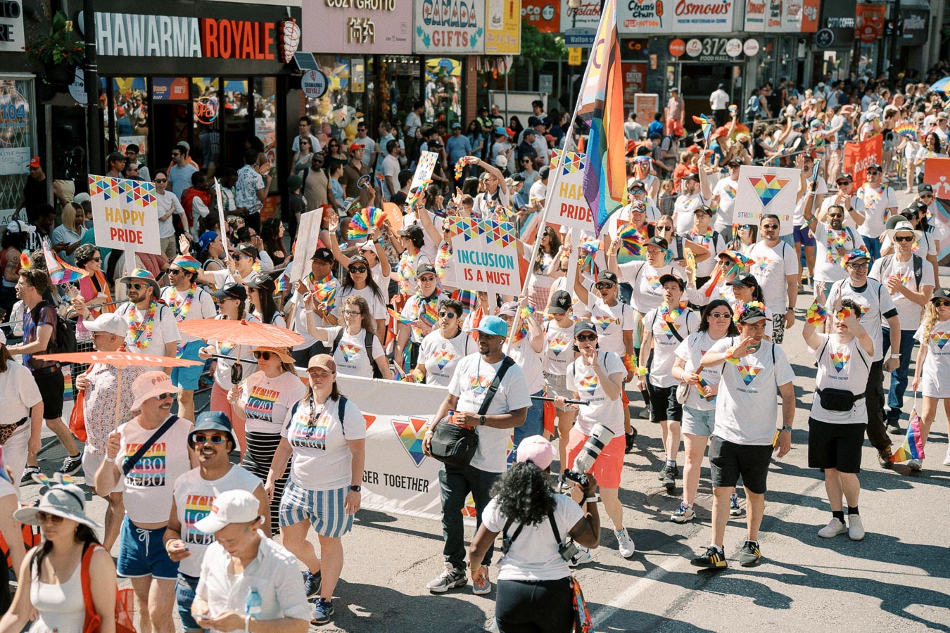 Participants in a Pride parade march down a city street, celebrating diversity and inclusion with colorful signs and attire.