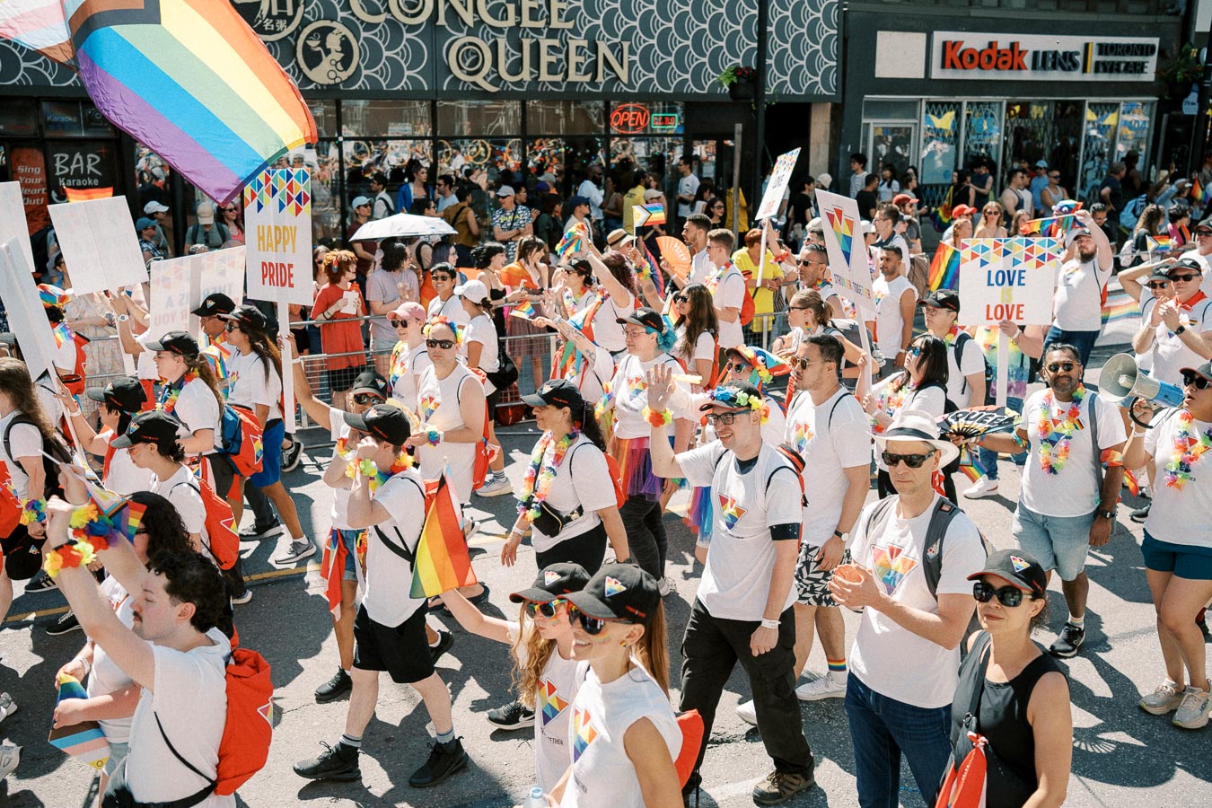Participants in a vibrant Pride parade march down the street, celebrating with rainbow flags and signs promoting love and equality.