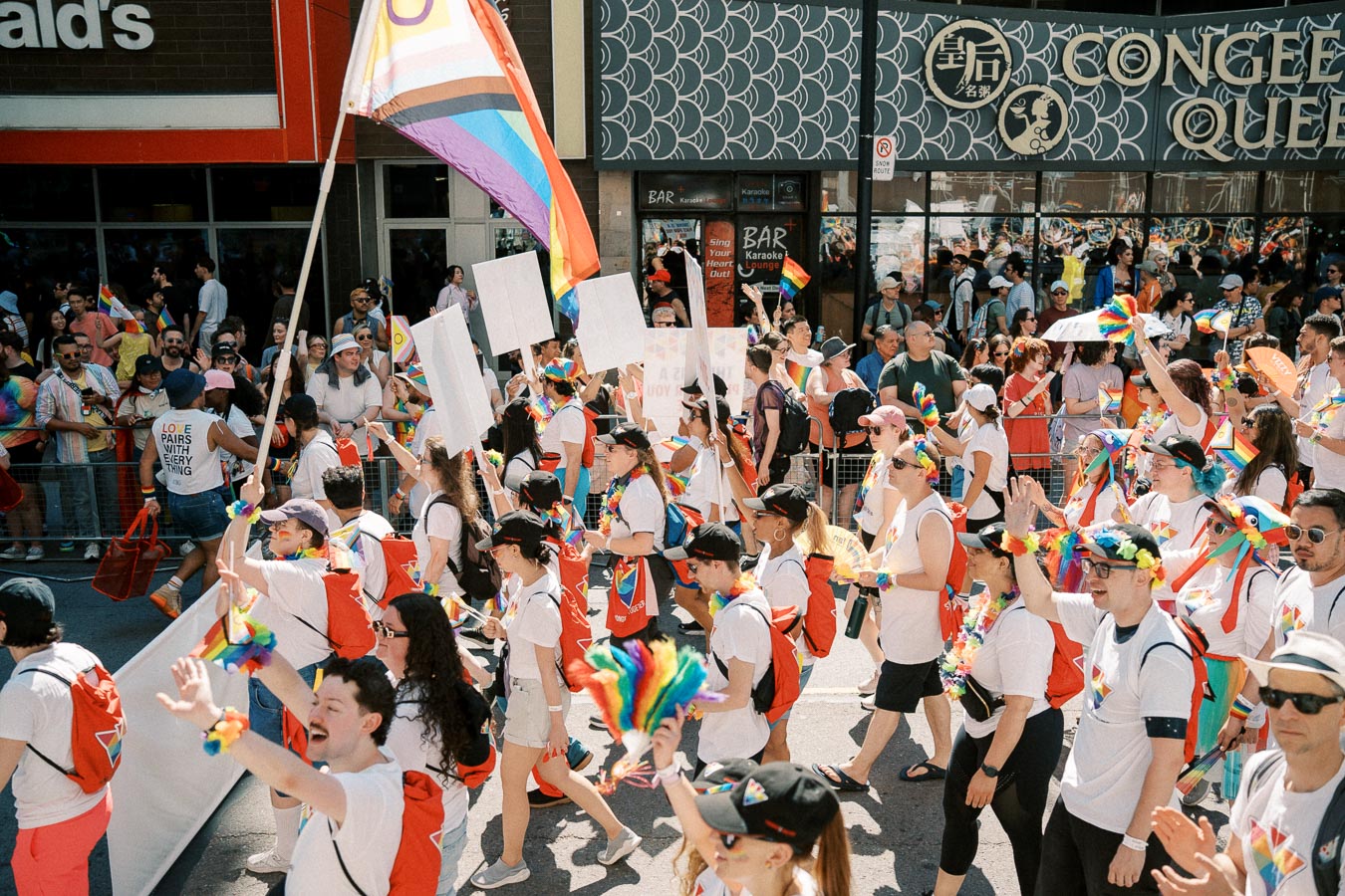 Participants in a pride parade march with colorful flags and signs, celebrating diversity and inclusion.