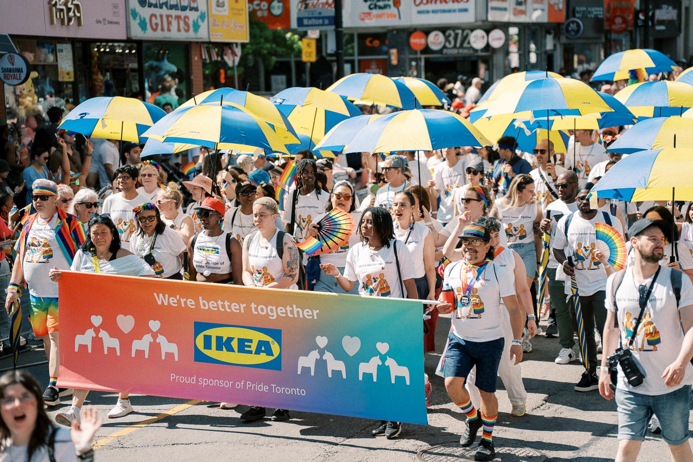 Participants in a Pride parade hold an IKEA banner reading 'We're better together', showcasing support for the LGBTQ+ community.