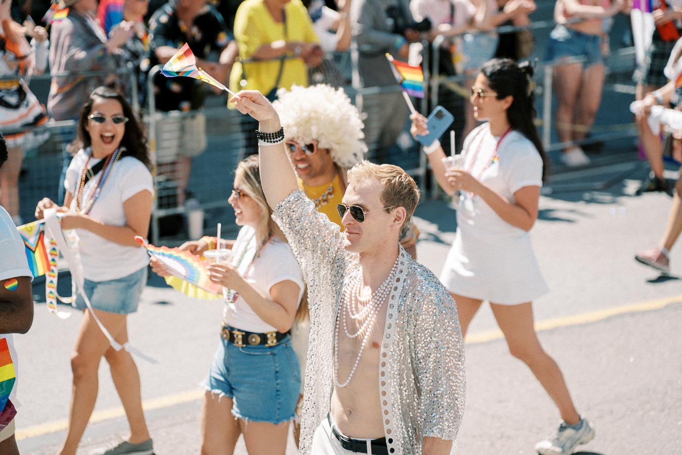 Participants at a pride parade joyfully wave rainbow flags and wear vibrant outfits, celebrating diversity and inclusion.