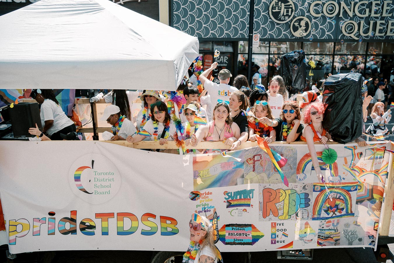 Participants at a Pride parade celebrate with colorful flags and banners, representing the Toronto District School Board.