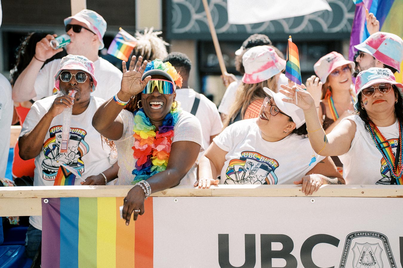 Participants at a pride parade joyfully wave rainbow flags and wear colorful attire, celebrating diversity and inclusion.