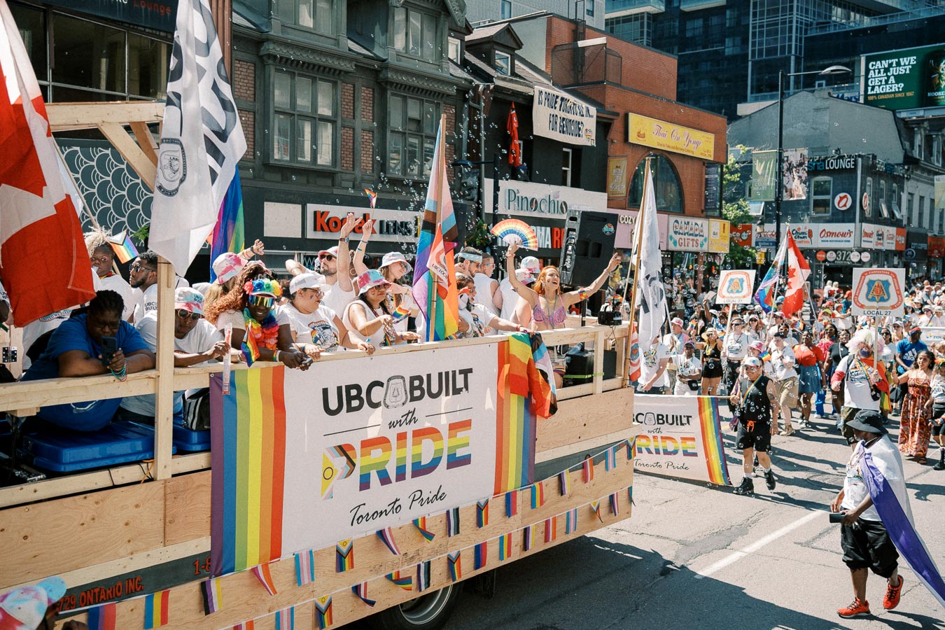 Participants celebrate on a float during the Toronto Pride Parade, showcasing a banner that reads 'UBC Built with Pride'.